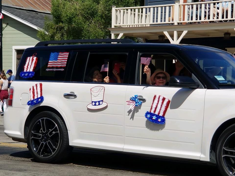 A car decorated with American flags and patriotic symbols participates in a parade.