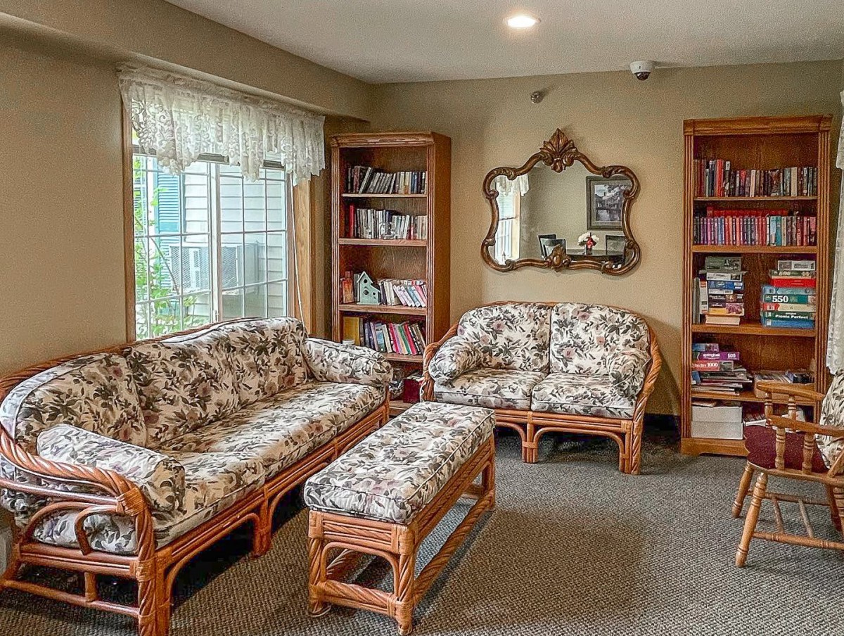 A cozy living room with patterned couches, bookshelves, and a mirror.