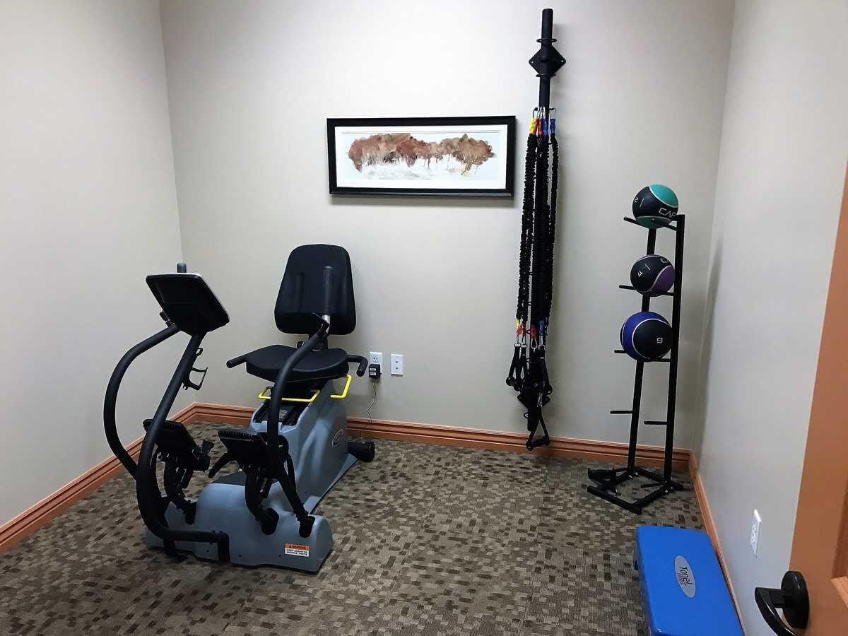 A small fitness room with an exercise bike, weights, resistance bands, and a yoga mat.