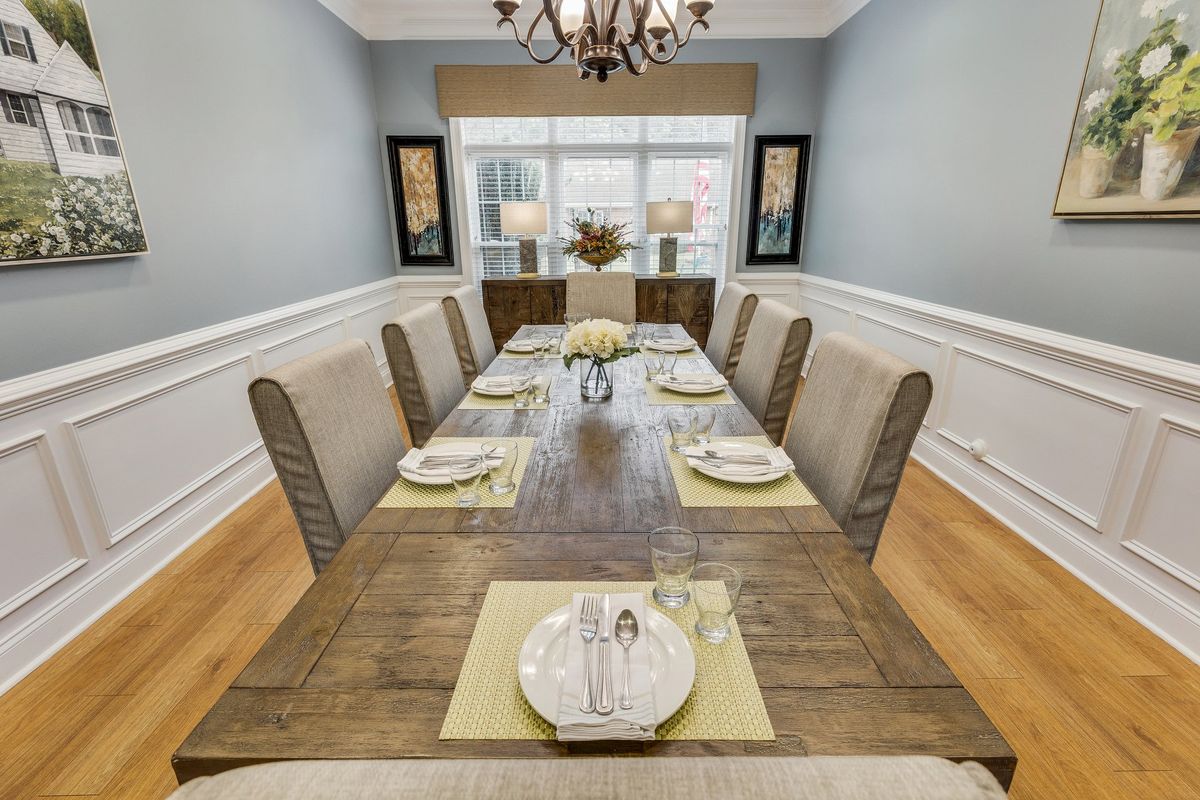 An elegantly arranged dining room with a long wooden table, upholstered chairs, and decorative place settings.