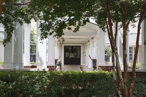 A view of a building entrance with white columns and greenery.