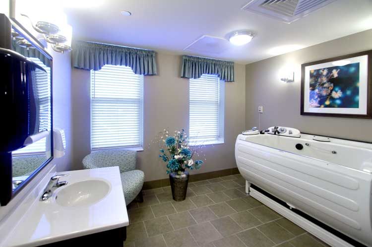 A modern bathroom with a bathtub, sink, tiled floor, and two windows with curtains.