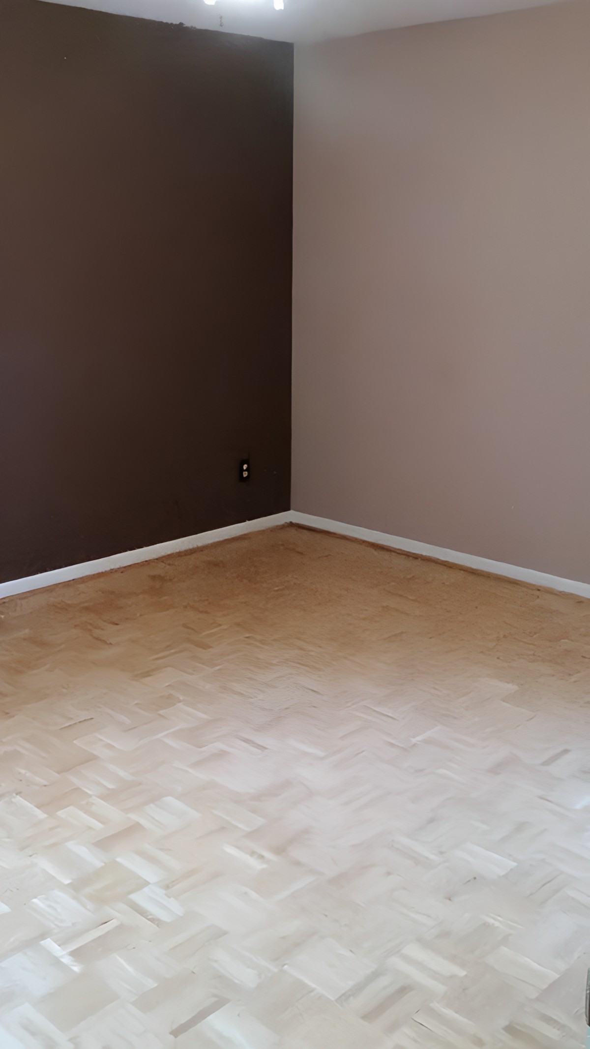 A minimalist empty room with two-tone brown walls and a light hardwood floor.