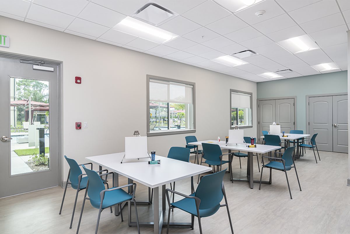 A modern office cafeteria with tables and chairs, featuring bright lighting and large windows.