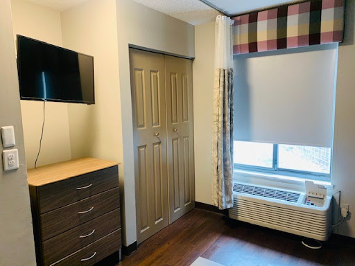 A cozy and modern room featuring a TV, dresser, and window with curtains.
