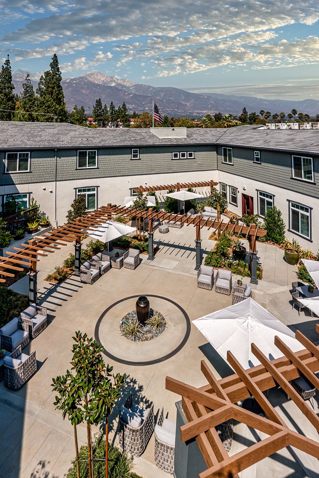 A modern courtyard with outdoor seating and pergolas, surrounded by a two-story building.