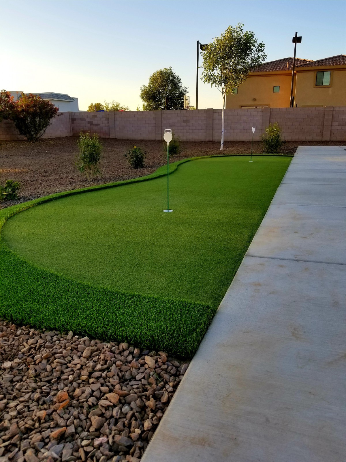 A backyard putting green with artificial grass next to a concrete area.
