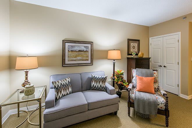 A cozy living room featuring a sofa, armchair, and decorative elements like lamps and a painting.