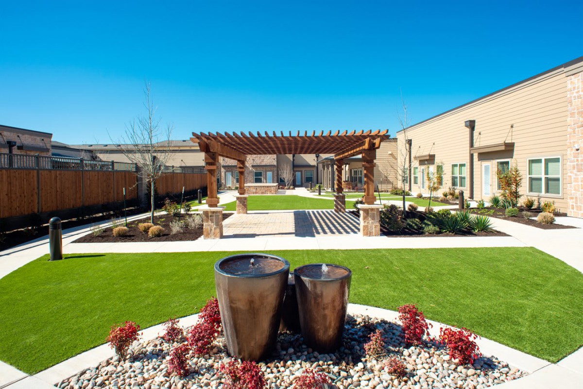 A beautifully landscaped garden with a pergola and water features under a clear blue sky.
