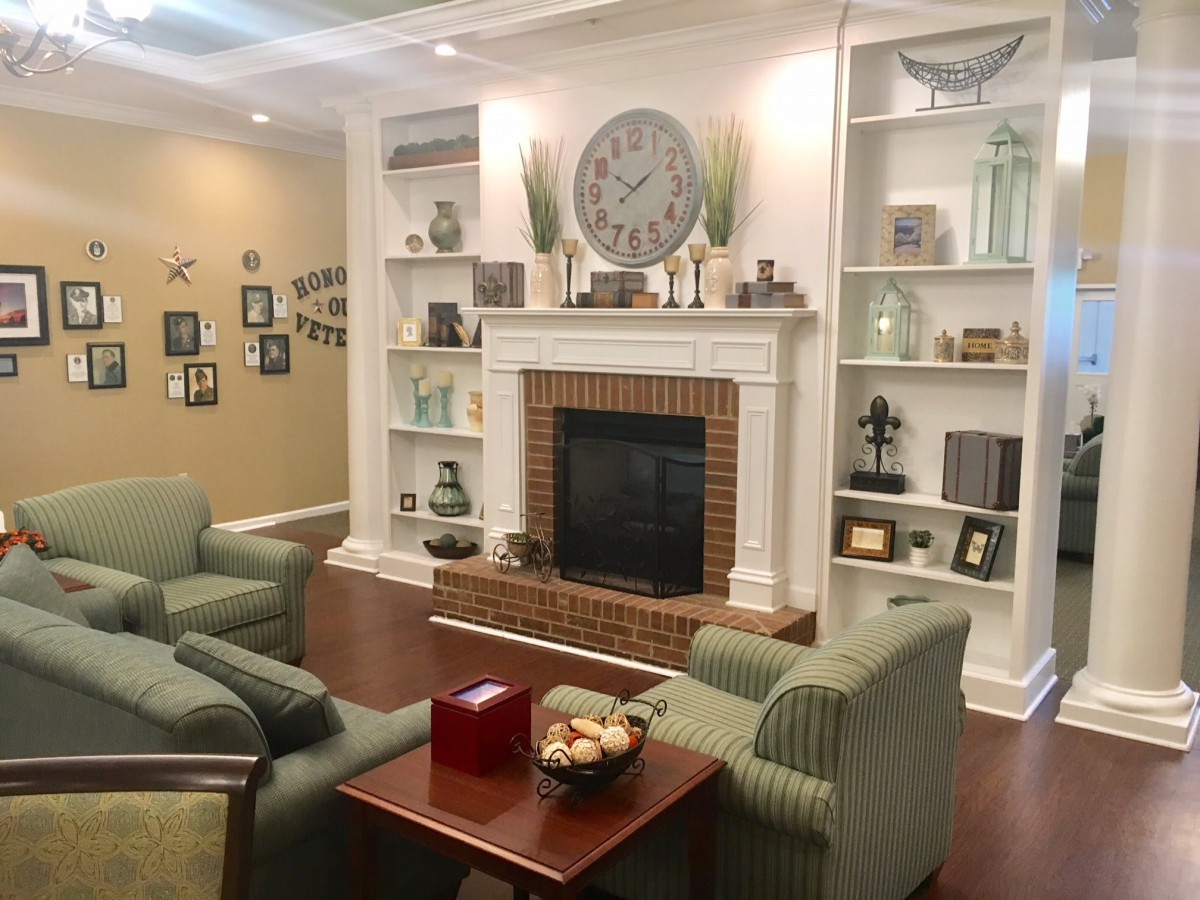 A cozy living room featuring a central fireplace surrounded by built-in shelves adorned with decorative items, comfortable armchairs, and a coffee table.