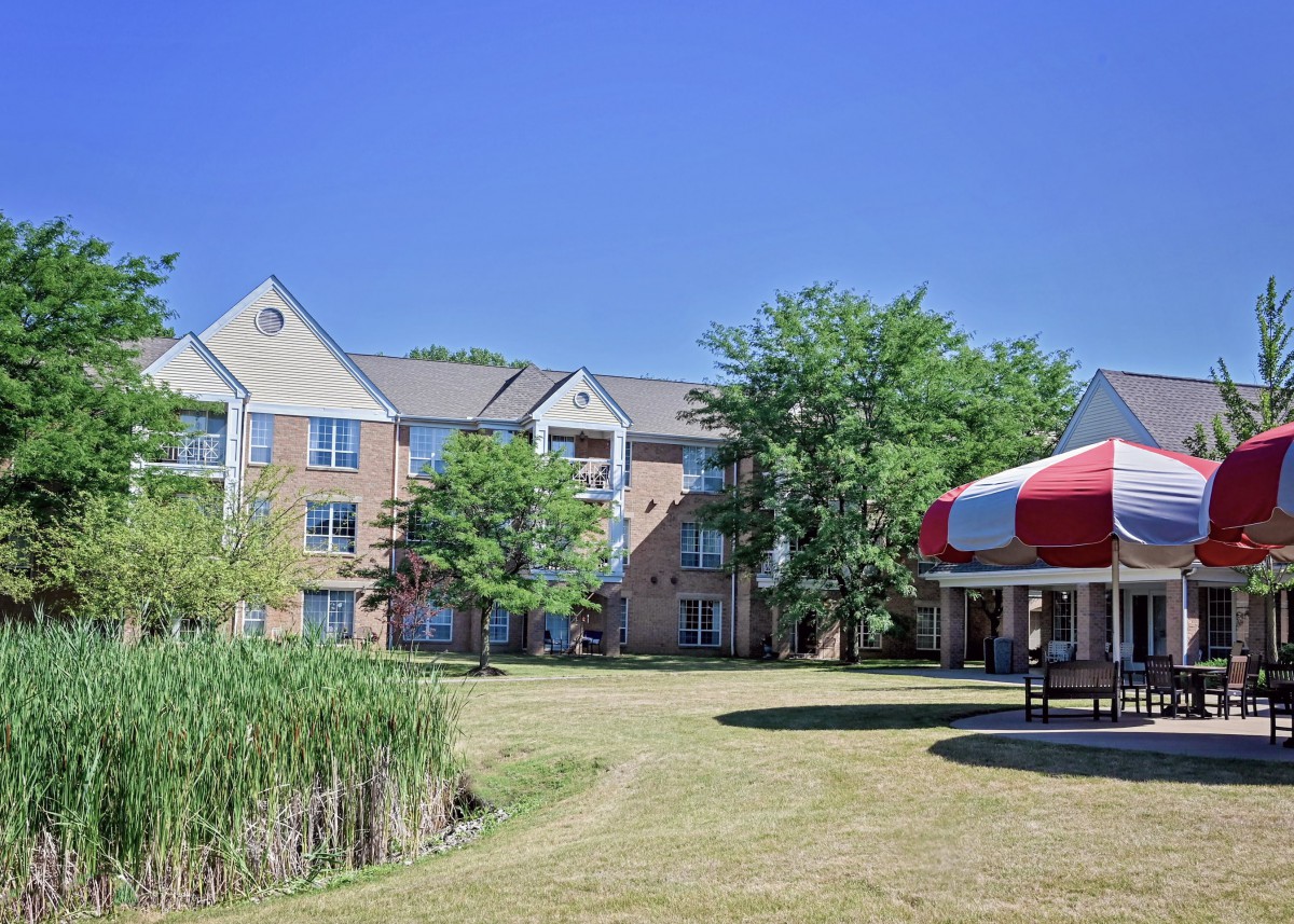 A residential building with a well-maintained lawn, surrounded by trees and featuring a gazebo under a clear blue sky.