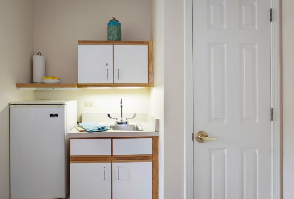 Compact kitchenette with white cabinets and a small fridge.