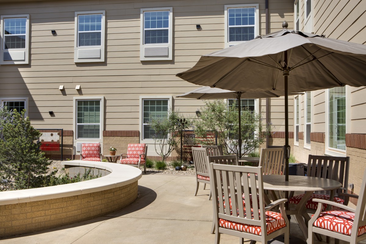 An outdoor patio area with chairs, tables, and umbrellas adjacent to a building.