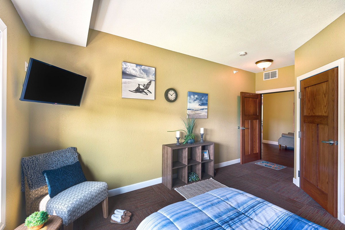 A cozy bedroom with green walls, featuring a bed, chair, wall-mounted TV, and decorative elements.