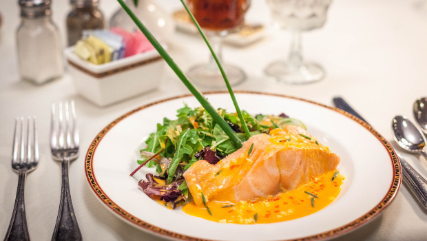 A plated dish of salmon topped with a creamy sauce, served alongside mixed greens and garnished elegantly.