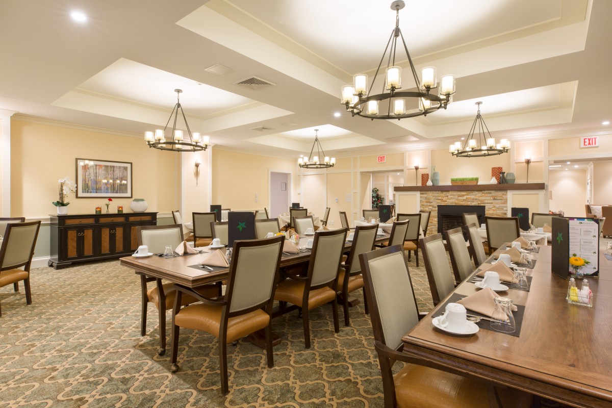 An elegant dining room with multiple tables and chairs, adorned with chandeliers and warm lighting.
