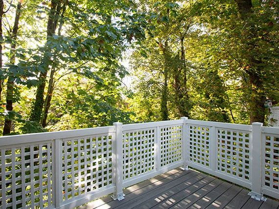 A tranquil deck with white lattice railings overlooking a lush, sunlit forest.