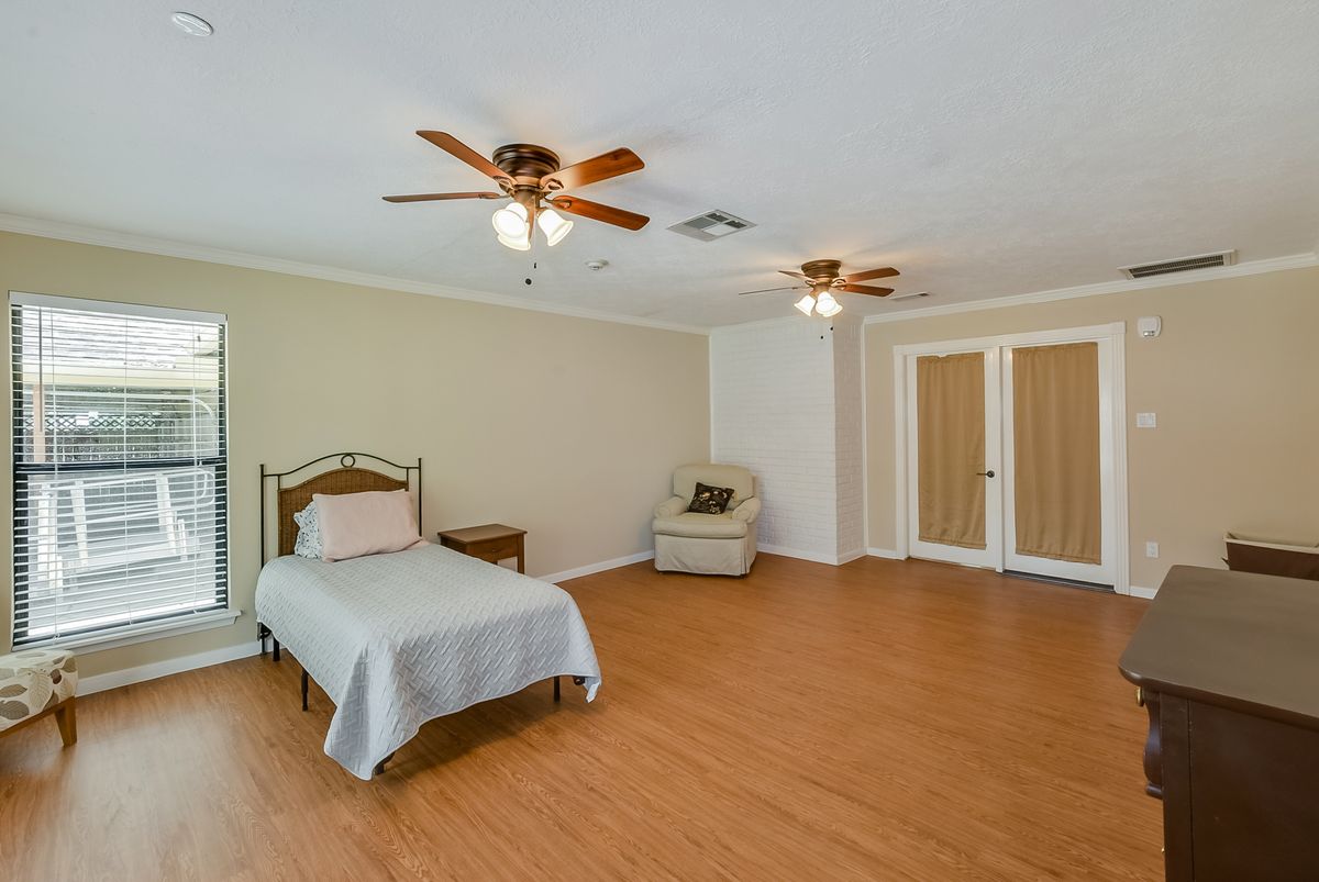 A spacious bedroom with a single bed and hardwood flooring, featuring two ceiling fans.