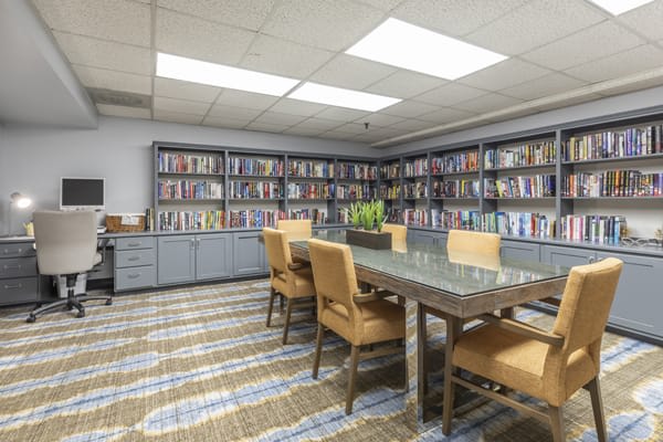 A cozy library room with bookshelves and a meeting table surrounded by chairs.