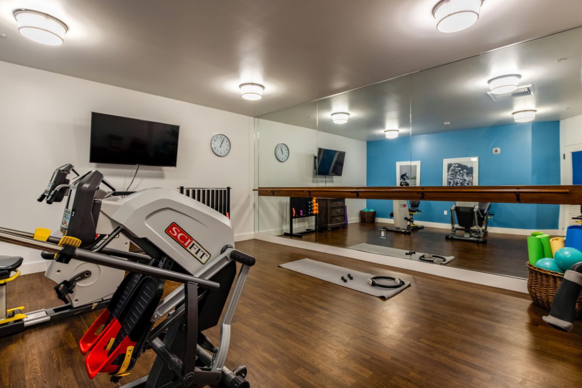 A modern gym room featuring exercise equipment, mirrors, and a wooden floor.