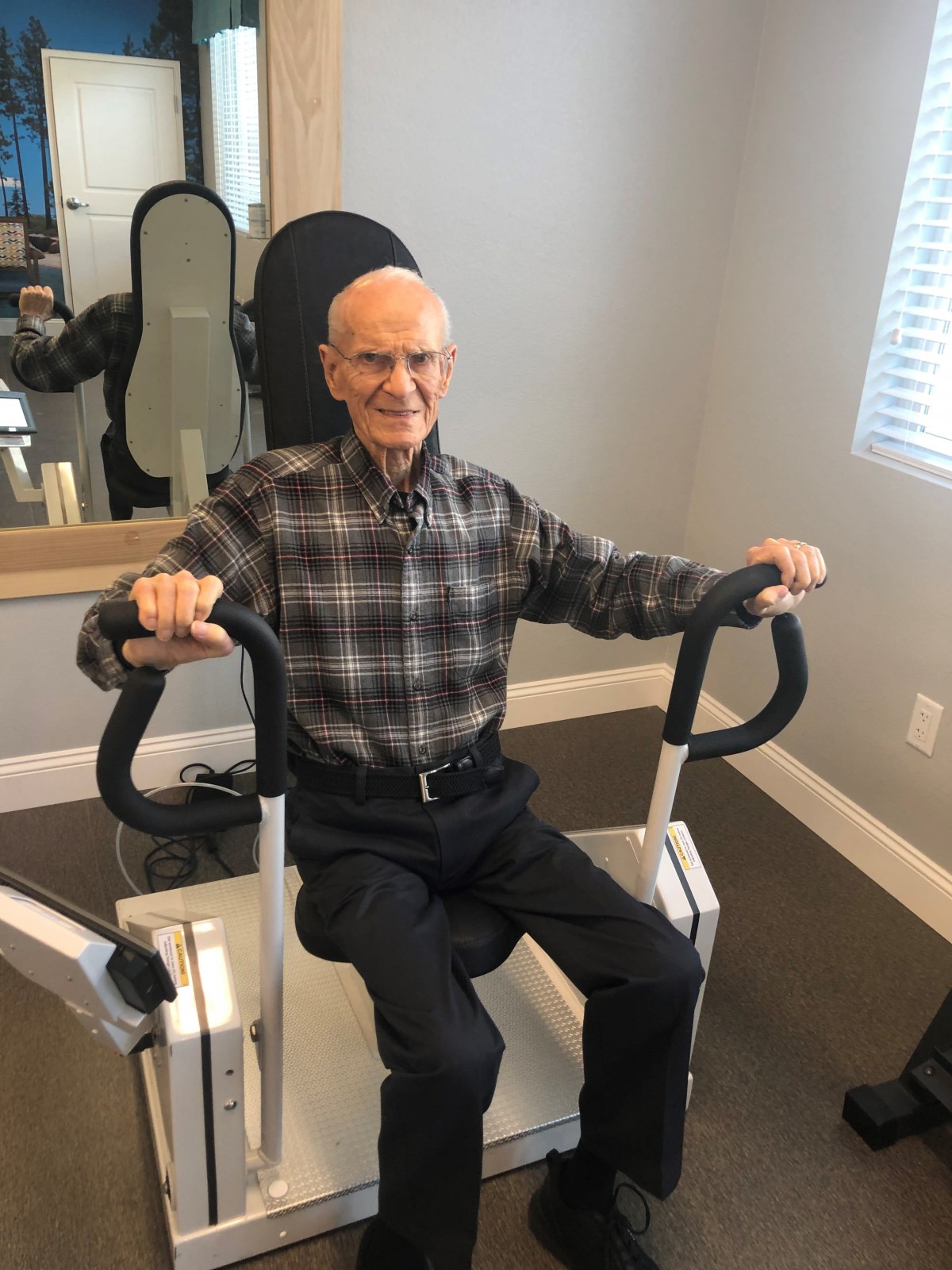 An elderly man exercising on a machine indoors.