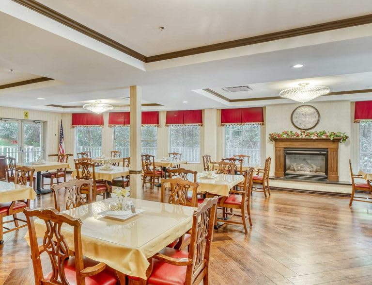 A spacious and elegant dining room with wooden tables and chairs, featuring a fireplace and large windows.