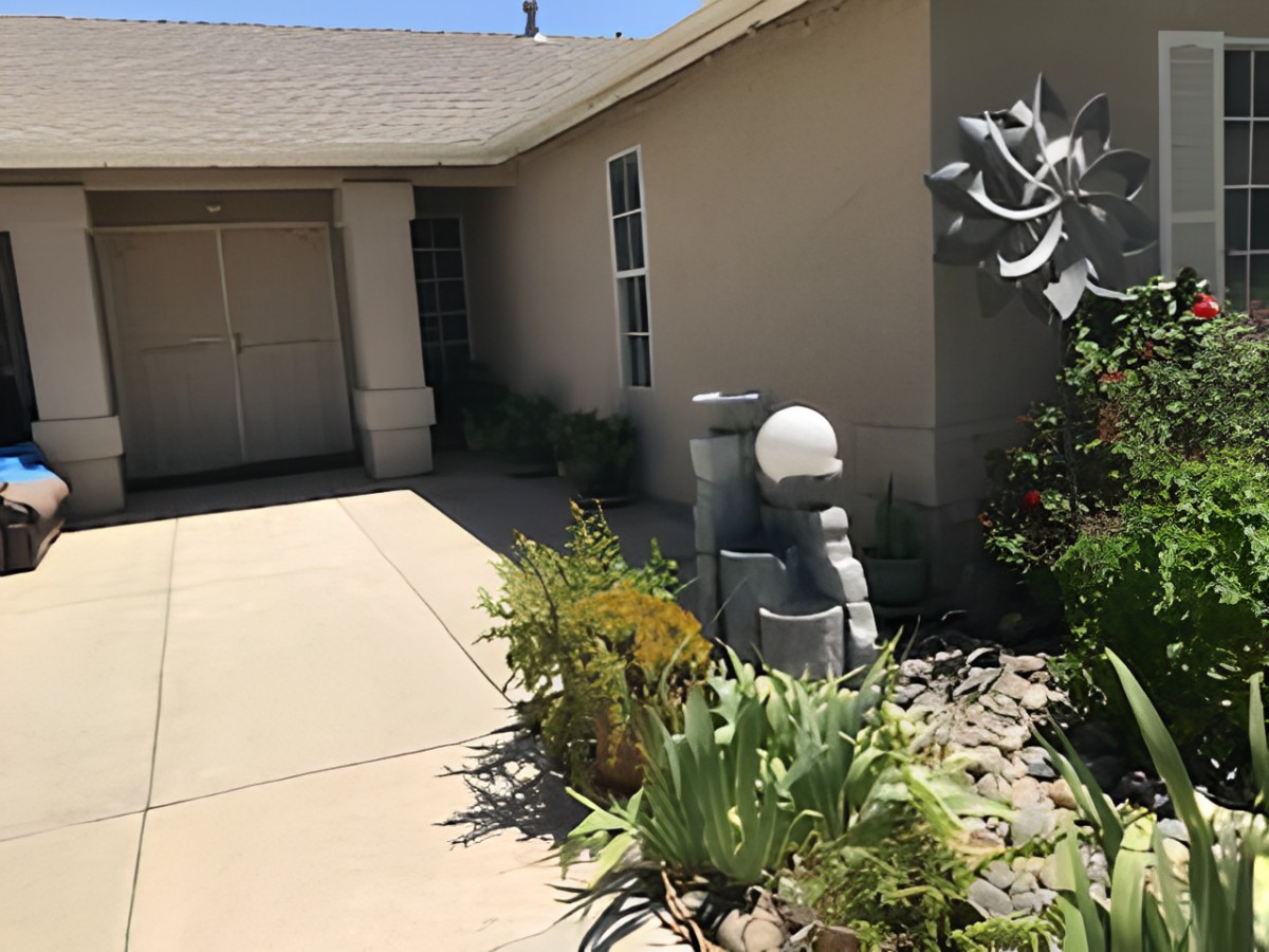 A modern house exterior featuring a well-maintained garden with various plants and a sculpture by the entrance.