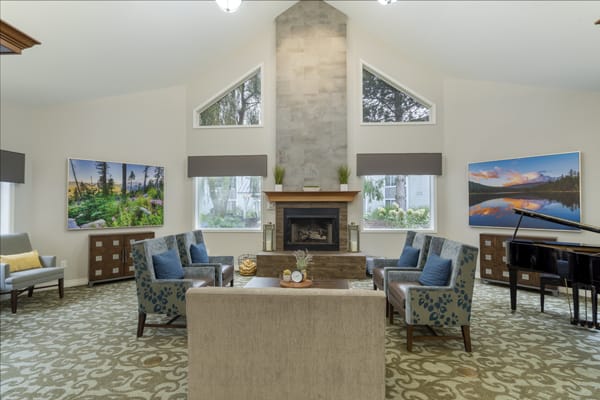 A spacious living room with a central fireplace surrounded by comfortable armchairs and large windows providing natural light.
