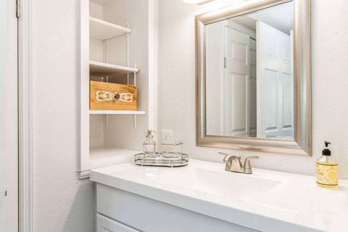 A clean and organized bathroom with a white countertop, mirror, and shelf storage.