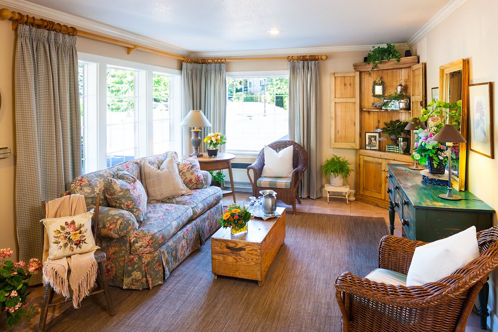 A cozy living room with a floral sofa, wooden coffee table, and large windows adorned with curtains.