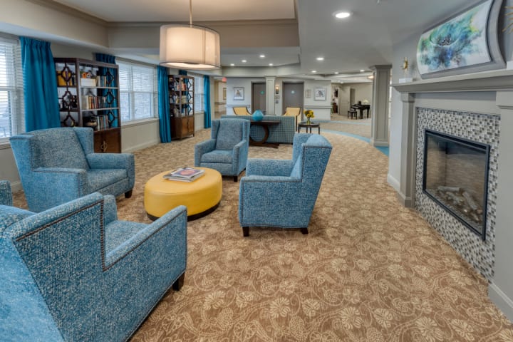 A modern living room with blue chairs, a yellow ottoman, and bookshelves.
