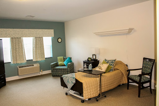 A well-furnished hospital room featuring a patient bed, a comfortable chair, and natural light from the window.