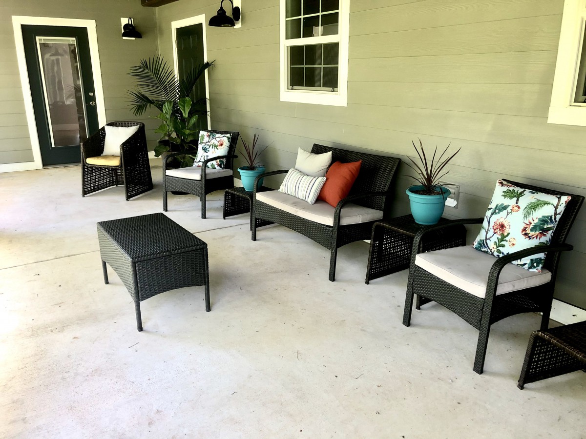 A cozy patio setup with outdoor furniture, including chairs, a sofa, a table, and decorative plants.