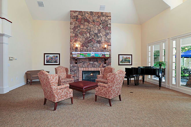 A cozy living room with armchairs around a fireplace and a piano in the corner.