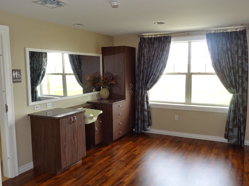 A well-lit interior room featuring a vanity, large windows with curtains, and polished wooden flooring.