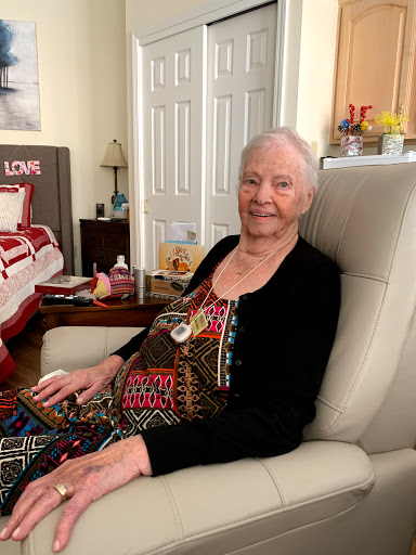 An elderly woman smiles warmly while sitting comfortably in her home.