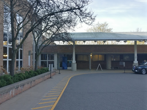A view of the entrance to a building with a parking area, surrounded by trees.