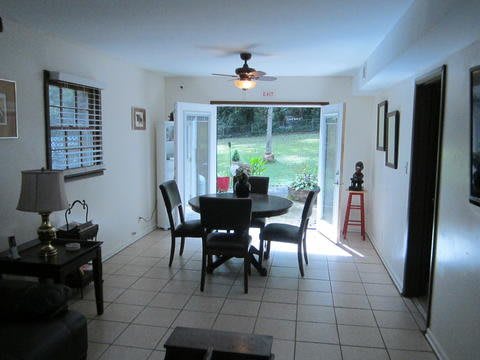 A bright dining room with tile flooring, featuring a table and chairs, large windows, and a ceiling fan.