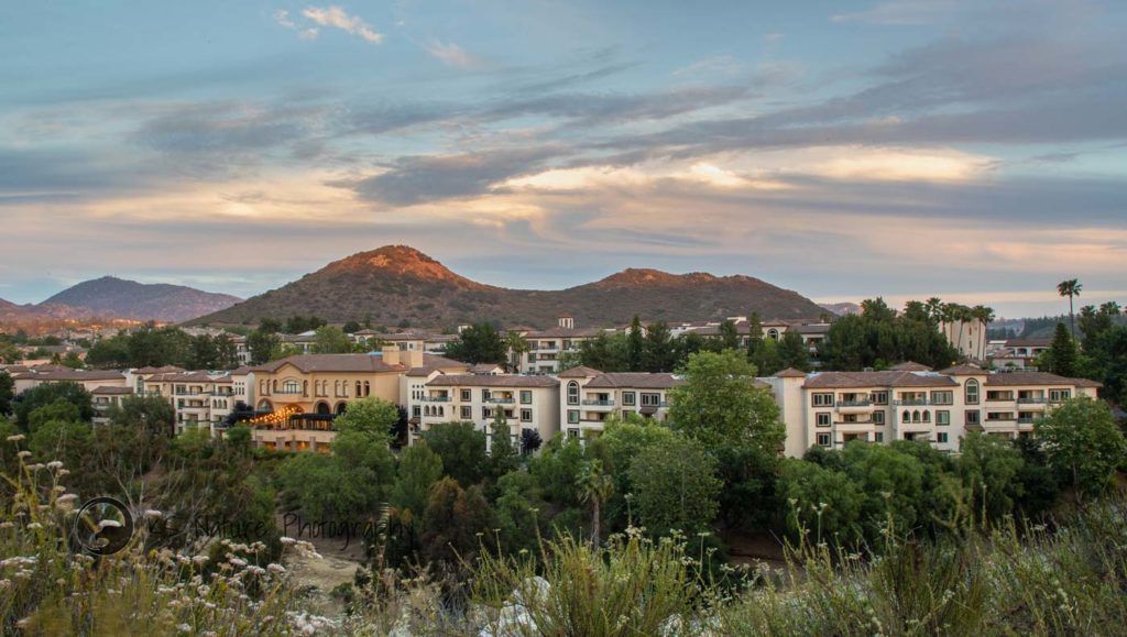 A scenic view of buildings nestled in a valley with mountains in the background during sunset.
