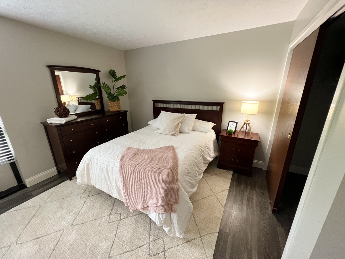 A cozy bedroom with a neatly made bed, dark wood furniture, and soft lighting.