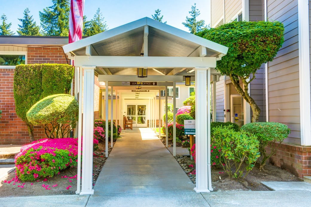 A covered walkway leading to the entrance of a building, surrounded by lush landscaping.