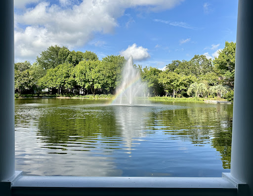 A serene park view featuring a fountain surrounded by lush greenery and a clear blue sky.
