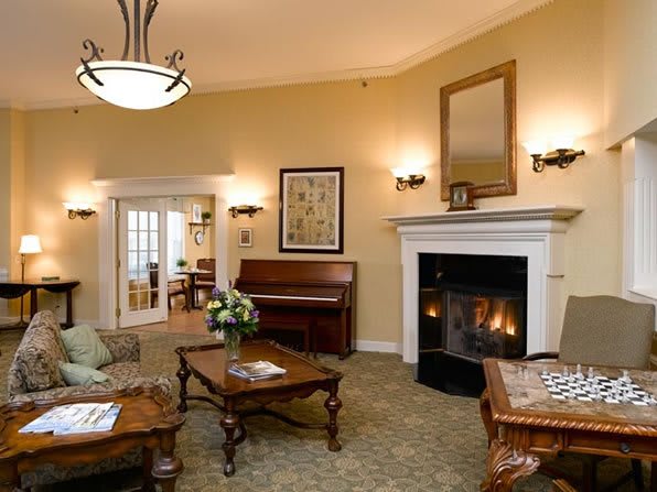 A cozy living room with a fireplace and a piano, featuring a sofa and coffee tables under a chandelier.