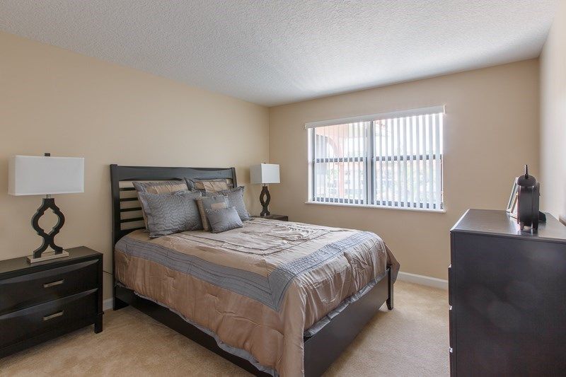 A simple and cozy bedroom with a neatly made bed, bedside lamp, and window blinds.