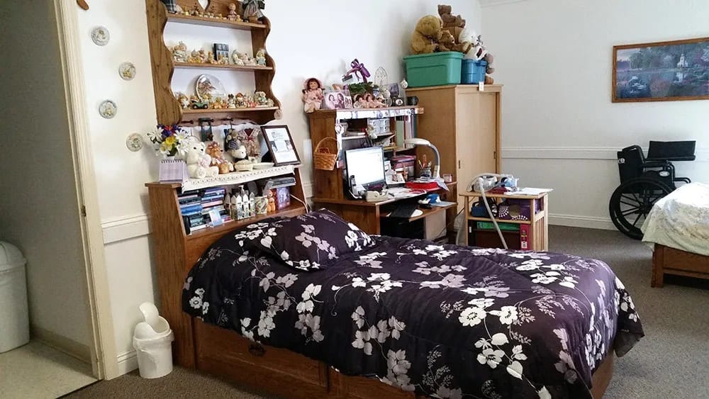 A cozy bedroom featuring a single bed with a floral bedspread, surrounded by shelves filled with decorations and stuffed animals.