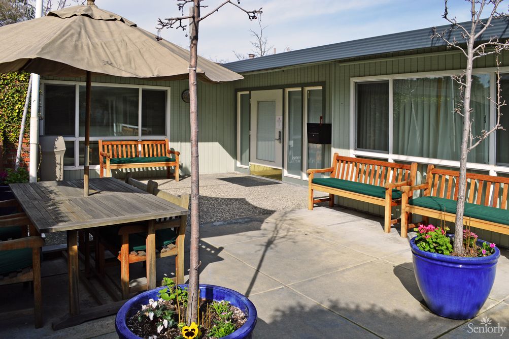 A cozy outdoor patio area with wooden benches, an umbrella, and potted plants.