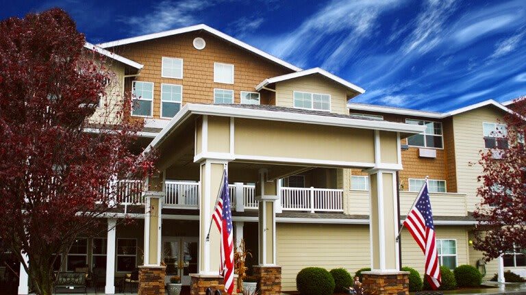 A multi-story residential building with an entrance covered by a large overhang, adorned with national flags.