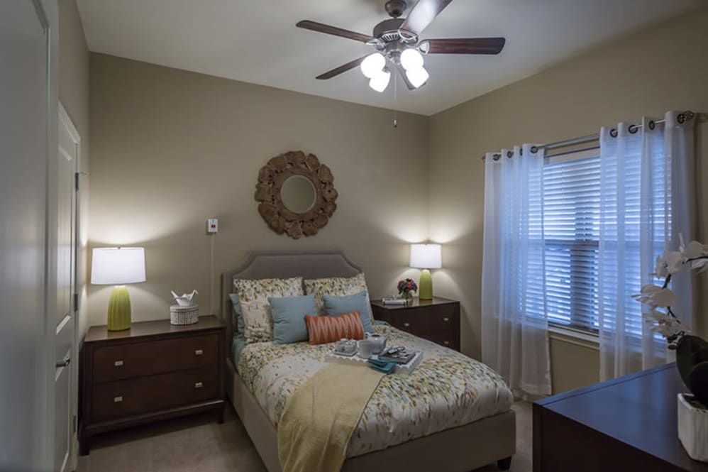 A cozy bedroom featuring a bed with decorative pillows, nightstands with lamps, and a ceiling fan.
