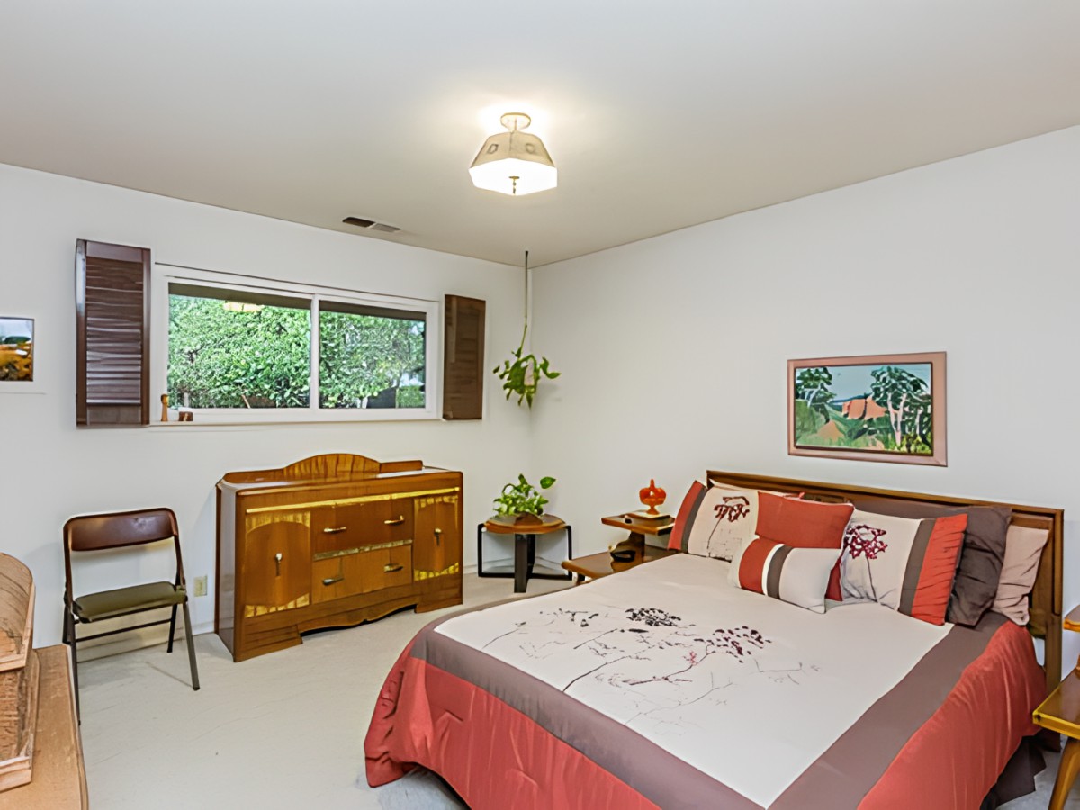 A cozy bedroom with a neatly made bed and a wooden dresser beside a window.