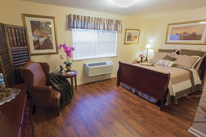 A cozy bedroom with wooden flooring, featuring a bed, chair, and decorative elements.